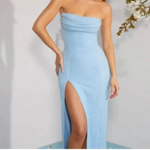 Ljusblå axelbandslös långklänning - Superfin ljusblå långklänning med axelbandslös design och hög slits på ena sidan. Klänningen har en tight passform och är perfekt för dig som vill sticka ut. Materialet ser ut att vara mjukt och lätt, vilket ger en snygg siluett.