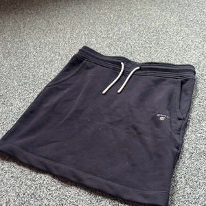 Svart kortkjol från Gant med snörning - Blå kortkjol från Gant med dragsko i midjan och diskret logga framtill. Mjuk och skön bomullskvalitet, klassisk design med fickor på sidorna och enkel att matcha. Den är i fint skick!