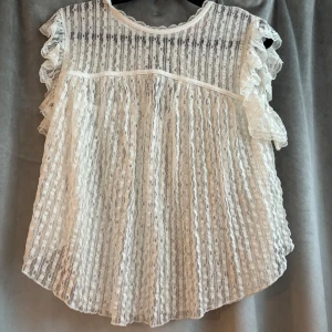 Vit spetsblus med volangärmar - Supersöt vit blus i spets med volangdetaljer på ärmarna och knytning i nacken. Super fin på och får att styla hur man vill. Aldig använd!