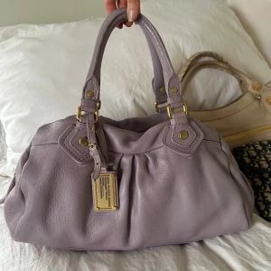 Ljuslila Q Classic Boston Bag! - OBS! Åker utomlands imorgon, sista dag jag kan skicka är idag. Köp gärna via min vinted @juliavallberg 🤎  Snyggaste ljuslila handväskan i nyskick från Marc by Marc Jacobs i äkta läder med gulddetaljer och dubbla handtag. Extremt välbevarad vintage modell! Perfekt för att ge en stilren touch till din outfit. Mått 40x22x15 cm (undersida). Kan hämtas hemma hos mig i Nacka eller skickas men kan tyvärr inte mötas🤍