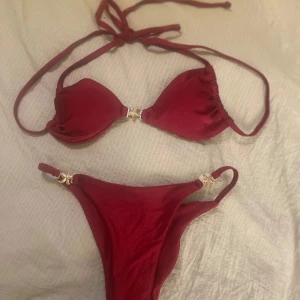 Vinröd bikini med gulddetaljer - Snygg vinröd bikini med knyt i nacken och dekorativa guldfärgade detaljer både på överdelen och underdelen. Perfekt för sommaren! Aldrig provad eller använd. Helt ny.