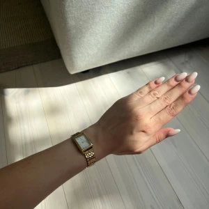 Guldplaterad vattentålig fyrkantig klocka  - Stilren klocka med fyrkantig urtavla i vitt och romerska siffror. Nyåris över 1000kr, helt ny fick den i PR bud, med låda som medföljer. Kan frakta inom 24h. Vattentålig och guldplatterad