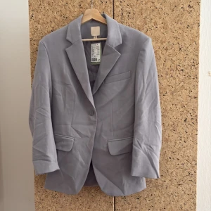 Ljusgrå kavaj från H&M XS - Snygg ljusgrå kavaj från H&M i storlek XS. Klassisk modell med slag, en knapp framtill och två fickor med lock. Perfekt för en stilren look och enkel att matcha med olika outfits. Aldrig använd!