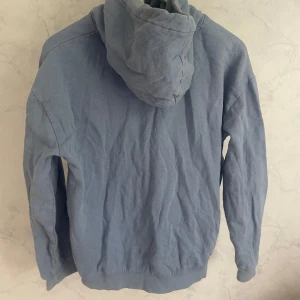 Blå hoodie - En basic blå hoodie med huva och dragsnören. Tröjan har en stor magficka framtill och ribbade muddar vid ärmslut och nederkant. 