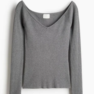 Grå ribbad långärmad tröja - Snygg grå ribbad tröja med v-ringad hals och lång ärm. Modellen är figurnära och har en djupare urringning som ger en trendig look. Perfekt att styla med jeans eller kjol för en clean och stilren outfit.