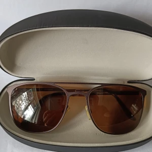 Bruna pilotbågar från Marc O'Polo - Snygga glasögon från Marc O'Polo med pilotformade bågar i metall och bruna tonade glas. Ramen är tunn och elegant, med näskuddar för extra komfort. Märkt Eschenbach Germany på insidan av skalmen. Perfekta för en cool och stilren look.