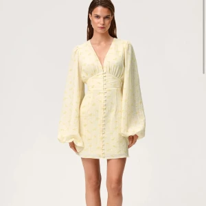 Ljusgul kortklänning med puffärm - Superfin ljusgul kortklänning med v-ringning, långa puffärmar och små blommiga detaljer. Klänningen har knappar framtill och markerad midja som ger en snygg siluett. Perfekt för sommarens alla tillfällen!