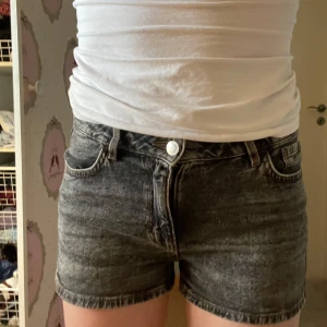 Svarta jeansshorts  - Snygga svarta jeansshorts från Lindex i tvättad denim-look. Modellen är midwaist med klassiska fem fickor, bälteshällor och knappgylf. Perfekta för sommardagar och passar till allt. Stilsäkra och bekväma shorts med en lite mörkare tvätt.