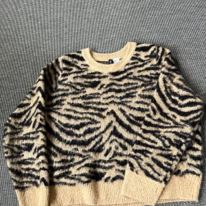 Ljusbrun zebramönstrad stickad tröja - Säljer en ljusbrun stickad tröja från H&M med svart zebramönster. Tröjan har rund halsringning, ribbade muddar och är långärmad. Däremot skulle jag säga att armarna är ganska korta, eftersom jag vanligtvis har storlek M men att den är lite för kort för mig i armarna. Perfekt för dig som letar efter en fin tröja med djurmönster!!