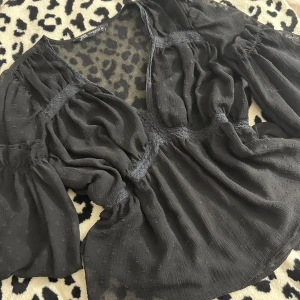 Svart blus från Zara - (PASSAR SOM ETT S) Supersnygg svart blus från Zara med v-ringning och transparenta partier. Blusen har lång puffärm, markerad midja och diskret rutstruktur i tyget. Luftigt material som ger en cool och trendig look. Perfekt att styla med jeans eller kjol. 
