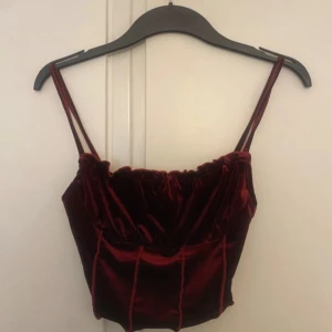 Vinröd sammets korsett-topp SHEIN - Supersnygg vinröd korsett-topp i sammet från SHEIN med dubbla smala axelband och markerade sömmar framtill. Croppad modell som ger en trendig vibe och passar perfekt till höga jeans eller kjol. Mjuk och glansig yta som fångar ljuset.
