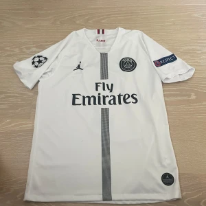 PSG Mbappé vit matchtröja Jordan - Snygg vit PSG fotbollströja med Mbappé 7 på ryggen, Fly Emirates-tryck och Jordan-logga. Kortärmad modell med Champions League och Respect-patchar på ärmarna. Tillverkad i lätt och ventilerande material, perfekt för fotboll eller att bära som supporter. Storleken L passar utmärkt om man har vanligtvis M. Pris kan diskuteras