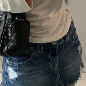 Y2k Denim Skirt - Trendiga blå jeansshorts med råa fransade kanter och slitna detaljer framtill. Klassisk femficksmodell med bälteshällor och knappstängning. Perfekta för en chill sommarlook och passar till allt från crop tops till hoodies.