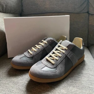 Grå sneakers i mocka och skinn - Stilrena grå sneakers med ovandel i mocka och skinn, beige snörning och klassisk gummisula. Snygg retrostil som passar perfekt till jeans eller dressade byxor. Låg modell med rund tå och diskreta detaljer.