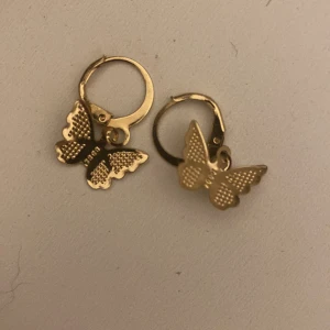 Guldiga örhängen med fjärilar - Snygga örhängen i guldton med hängande fjärilar. Fjärilarna har fina detaljer och ger ett lekfullt och trendigt intryck. Perfekta för dig som vill ha något unikt och gulligt i öronen. Passar till alla tillfällen när du vill sticka ut lite extra.