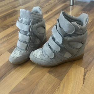 Nya Isabel Marant-liknande skor i mocka. - Snygga grå sneakers med inbyggd kilklack och breda kardborreband. Skorna är gjorda i mjuk mocka och har en cool, sportig design med perforerade detaljer på tån och vadderad kant. Perfekta för dig som vill ha lite extra höjd men ändå en streetstyle-look. Ser exakt ut som Isabel Marants! Skorna ser helt NYA ut och det finns inga täcken på användning. Säljer då dem inte passar 💕💕