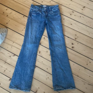 Blå bootcut jeans med utsvängda ben - Snygga blå jeans med bootcut-modell och klassisk femficksdesign. Jeansen har normal midja och är tillverkade i ett mjukt denimtyg som ger en skön passform. Perfekta för dig som gillar en retroinspirerad look med utsvängda ben.