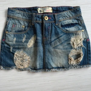  jeanskjol  - Kort jeanskjol från Terranova med slitna detaljer och fransig nederkant. Klassisk blå denim med fem fickor och bälteshällor. Snyggt trasiga partier framtill för en edgy look.