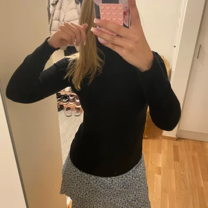 Svart polotröja i tight passform - Svart polotröja med lång ärm och tight passform. Hög krage som sitter snyggt runt halsen och ger en clean look. Perfekt att styla med kjol eller jeans. Mjuk och stretchig, passar dig som gillar en enkel men stilren vibe.