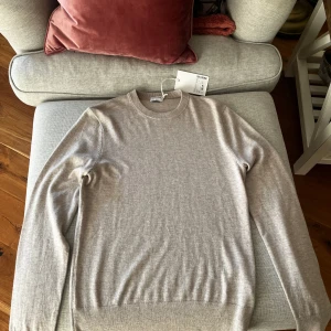 Beige merinoulltröja från Filippa K - Supersnygg beige tröja från Filippa K av merinoull. Enkel och stilren design med rund halsringning och långa ärmar. Perfekt för lager-på-lager och funkar året runt. Färgen är en ljus beige melange som är lätt att matcha. Tröjan passar även S
