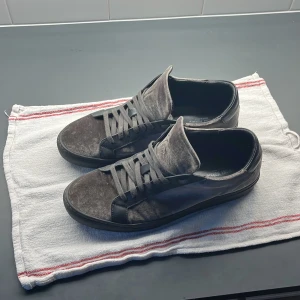 Grå sammetssneakers från Antony Morato - Snygga sneakers från Antony Morato i grå sammet med svarta detaljer i skinn. Skorna har rund tå, platt sula och klassisk snörning. Perfekt för dig som vill ha en stilren men ändå unik look. Tillverkade i Italien.