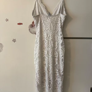 Vit spetsklänning från NLY One - Supersnygg vit spetsklänning från NLY One med smala axelband och v-ringning både fram och bak. Klänningen är figurnära och har ett vackert blommigt spetsmönster som ger en romantisk vibe. Perfekt för dig som vill sticka ut med en elegant look.