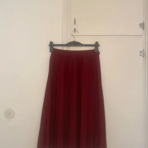 Mörkröd långkjol med resårmidja - Snygg mörkröd långkjol med mjukt fall och resår i midjan. Kjolen är enkel och stilren utan mönster, perfekt för dig som gillar en clean look. Materialet känns lätt och flowy, vilket gör den superbekväm att bära.