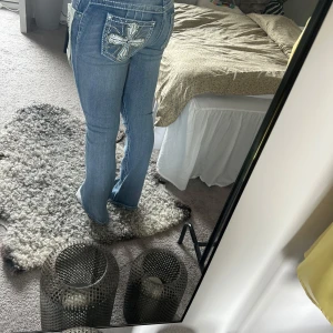 Sky ljusblå jeans med broderade fickor - Ljusblå jeans från Sky med snygga broderade kors och nitar på bakfickorna. Modellen har låg midja och bootcut-snitt som ger en retro vibe. Jeansen är i klassisk denim och har coola detaljer som kontrastsömmar och slitningar.
