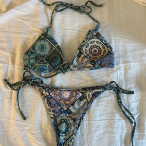 Mönstrad bikini med knyt - Snygg bikini med mandala-inspirerat mönster. Klassisk trekantsmodell med knyt både upptill och i sidorna på underdelen. Storlek s i båda delarna. Kupan skulle jag säga är en C💚💙