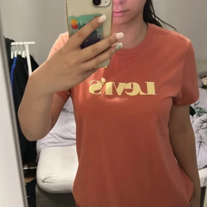 Rostfärgad Levi's t-shirt i bomull - Snygg rostfärgad t-shirt från Levi's med klassisk logga i gult framtill. Modellen är rak med rund hals och korta ärmar. Tillverkad i mjuk bomull som känns skön mot huden. Perfekt för dig som gillar en enkel men stilren look.