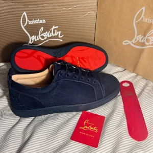 Mörkblå sneakers från Christian Louboutin - Snygga mörkblå sneakers från Christian Louboutin i mocka med ikonisk röd sula. Skorna har rund tå, platt sula och ton-i-ton broderad logga på hälen. Klassisk snörning och lyxig känsla, perfekt för dig som vill sticka ut med exklusiva detaljer. Obs lnte 0rglnal 