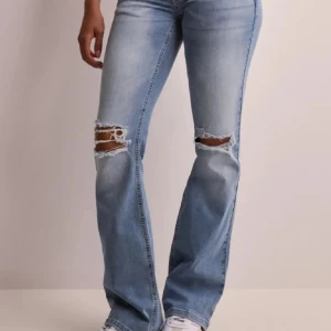 Ljusblå bootcut jeans från Nelly  - Snygga ljusblå jeans med bootcut passform och slitna hål över knäna. Låg midjade och klassiska bakfickor med lock och knapp. Jeansen har en trendig tvätt och är perfekta för en avslappnad streetstil.