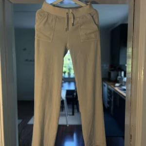 Beiga mjukisbyxor Juicy Couture S - Supermysiga beiga mjukisbyxor från Juicy Couture med snören i midjan om de sitter för löst och stora fickor fram. Byxorna har raka ben och bakfickor med knappdetalj. Perfekta för dom dagar du vill ha myskväll 