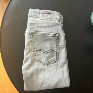 Replay jeans  - Säljer ett par ljusgrå jeans från Replay med klassisk femficksdesign och raka ben. Jeansen har snygga detaljer vid fickorna och en diskret Replay-logga. Perfekt för dig som gillar en clean och stilren look.