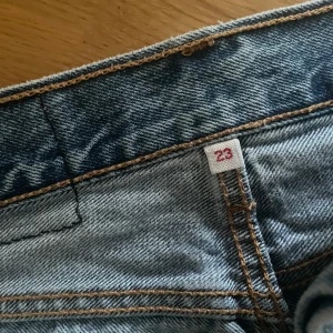 Levi's jeanskjol med fransig kant - Säljer en klassisk blå jeanskjol från Levi's med rå, fransig nederkant och knappar framtill. Kjolen har fem fickor, bälteshällor och den ikoniska Levi's-lappen bak. Perfekt för dig som gillar en avslappnad och cool stil.