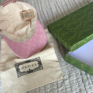 Rosa Gucci keps med GG-mönster - Exklusiv rosa keps från Gucci med ikoniskt GG-monogram i hela tyget. Kepsen har justerbart spänne bak i rosa läder och kommer med original dustbag och grön Gucci-box. Tillverkad i bomull och polyester för en lyxig känsla och snygg passform.