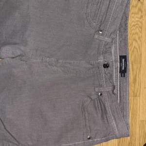Grå chinos från Dressmann - Snygga grå chinos från Dressmann med klassisk femficksdesign och raka ben. Byxorna är tillverkade i mjuk bomull och har normal passform. Perfekta för en clean och stilren look. Aldrig använda helt nya  fick i present men för små  köparen kommer att märka det när varan är framme o dags för användning ☀️