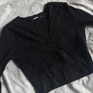 Svart omlott tröja  Bik Bok - Säljer en svart ribbad omlotttröja från Bik Bok i storlek XS. Långärmad croppad passform. Mjukt matrial, sitter smickrande då den har som ett lite tightare band runt midjan. Skriv för fler detaljer!