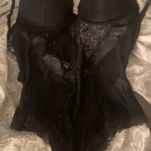 Svart spetsig body från H&M - Supersnygg svart body från H&M med vadderade kupor och detaljer i spets. Axelbanden är justerbara och bodyn har knäppning i grenen. Materialet är mjukt och stretchigt med transparenta partier och spetskant nertill. Perfekt för att lyfta din outfit med en edgy vibe. Nytt pris : 360kr