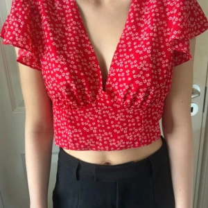 Röd blommig croppad blus - Superfin röd blus med små vita blommor, djup v-ringning och korta, luftiga ärmar. Croppad modell med smock baktill som ger en snygg passform. Skriv vid intresse! 🌸