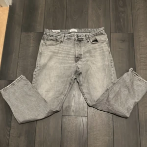 Grå jeans från Jack & Jones (pris kan diskuteras) - Snygga grå jeans från Jack & Jones med stentvättad look. Klassisk femficksmodell med raka ben och normal passform. Jeansen har bälteshällor, knapp och dragkedja i gylfen samt läderpatch bak i midjan. Perfekta till en everyday look.