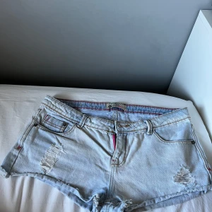 Ljusblå jeansshorts med slitningar - Snygga ljusblå jeansshorts från Terranova med slitna detaljer och råa kanter. Shortsen har rosa sömmar och dragkedja, samt coola fickor med rosa detaljer bak. Perfekta för sommardagar när du vill ha en avslappnad och trendig look.