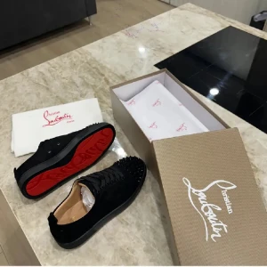 Svarta sneakers från Christian Louboutin - Snygga svarta sneakers från Christian Louboutin med klassisk röd sula och coola nitar på tån. Skorna är i mocka och har snörning framtill. Perfekta för dig som vill sticka ut med en lyxig och edgy stil.