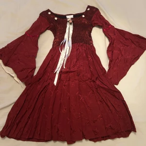 Vinröd barnklänning från Minisa - Supercool vinröd klänning från Minisa med vida ärmar och blomdetaljer. Blomman i mitten sitter fast med en säkerhetsnål. Storlek M i barnstorlek