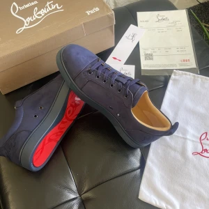 Blå mocka sneakers från Louboutin - Snygga sneakers från Christian Louboutin i mörkblå mocka med klassisk röd sula och diskret logga på sidan. Skorna har rund tå, snörning och en lyxig känsla med beige innersula. Perfekta för dig som vill sticka ut med exklusiv stil. Helt nya aldrig använda eller testade. 10/10 skick. Allt ingår 