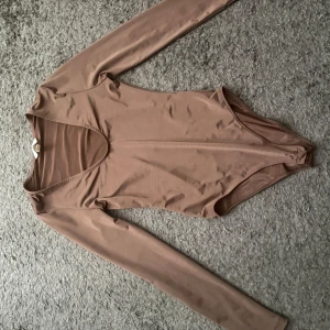 Beige långärmad bodysuit H&M XS - Säljer en beige långärmad bodysuit från H&M i storlek XS. Bodyn har djup v-ringning och är tillverkad i ett mjukt, stretchigt material. 