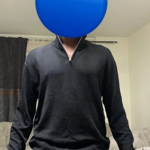 Svart stickad tröja med half zip - Svart stickad tröja med halv dragkedja i halsen. Tröjan har lång ärm, ribbade muddar och en clean, enkel look som passar till många outfits. Perfekt för dig som gillar stilren och bekväm design.