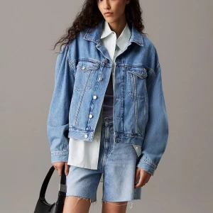 Oversized blå jeansjacka - Säljer en oversized blå jeansjacka med klassisk krage och silverfärgade knappar. Jackan har två bröstfickor med lock och knapp. Perfekt att slänga över en hoodie eller skjorta för en avslappnad stil. Från Calvin Klein väldigt fint bra skick, nypris 1800kr