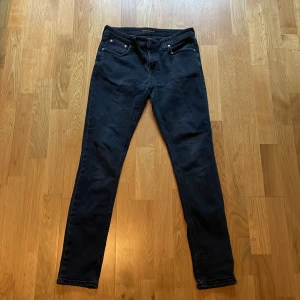 Svarta skinny jeans från nudie jeans - Säljer ett par svarta slim fit jeans från Nudie jeans. Normal midja. Jeansen är i stretchigt bomullsmaterial som sitter tajt men bekvämt längs benen. Storleken är 31/32, jag själv är 170 och därför är lite stort på baksidan men sitter nog perfekt en storlek högre. En personlig favorit tycker jag och tveka inte att fråga frågor. Svarar så fort jag kan!
