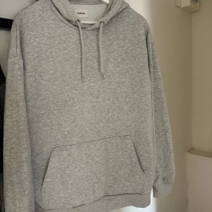 Grå hoodie från Yourturn - Säljer en stilren grå hoodie från Zalando/Yourturn med huva och snörning. Tröjan har en stor magficka och ribbade muddar vid ärmslut och nederkant. Perfekt för chill dagar eller när du vill ha en enkel och clean look.